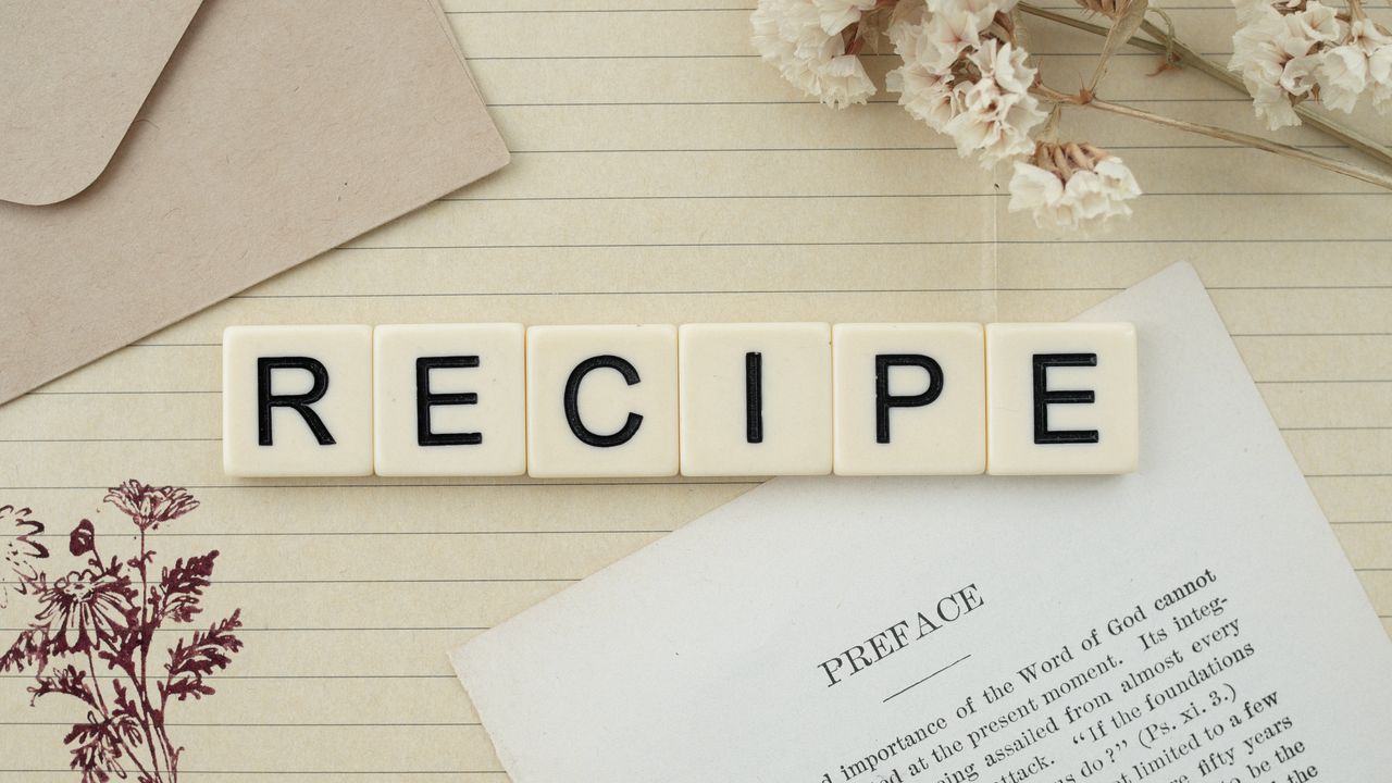 Elegant flat lay featuring recipe letter tiles, dried flowers, and notes on lined paper.